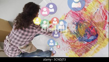 Artist wearing apron kneeling and painting on paper in studio with brushes, AR overlays, copy space Stock Photo