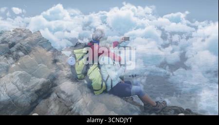 Taking selfie mature hiking couple leaning on coastal edge, with smartphone, backpacks and poles Stock Photo