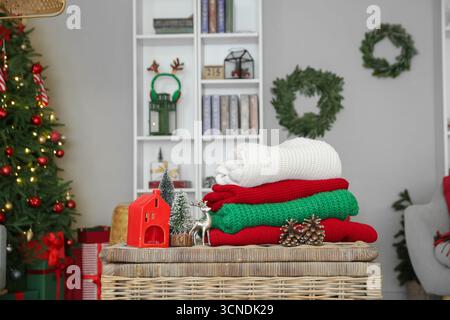 Stack of winter clothes with Christmas decorations on wicker table at home Stock Photo