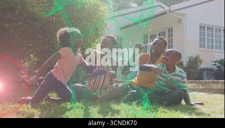 Family of four playing with bubbles on front yard lawn, with father using bubble wand Stock Photo
