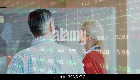 Analyzing coworkers studying data projection on transparent board in office, with sticky notes Stock Photo