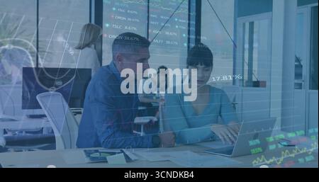 Collaborating professionals analyzing financial data overlays in open-plan office, with laptop Stock Photo