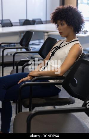African american woman sitting in boardroom by office chairs, table, frosted windows, copy space Stock Photo