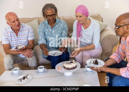 Diverse friends sharing chocolate cake on white coffee table in living room with cups Stock Photo