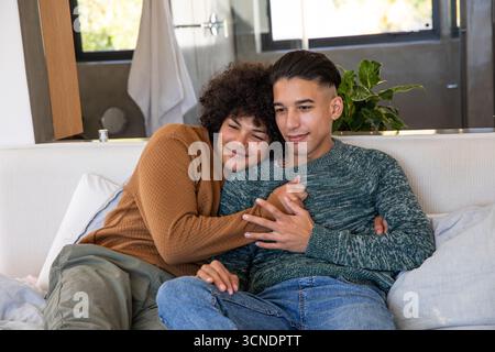 Two men sitting closely on light-colored sofa with large wall mirror in modern living room Stock Photo