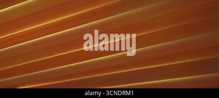 An abstract close-up of pleated material forming a rhythmic pattern of diagonal stripes. The warm copper fabric has a fine texture, with glowing golde Stock Photo