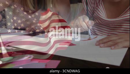 Painting mother and daughters using paintbrushes on paper at home dining table, with flag overlay Stock Photo