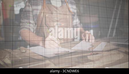 Sketching craftsman wearing leather apron drawing plans on paper at studio bench, with grid overlay Stock Photo