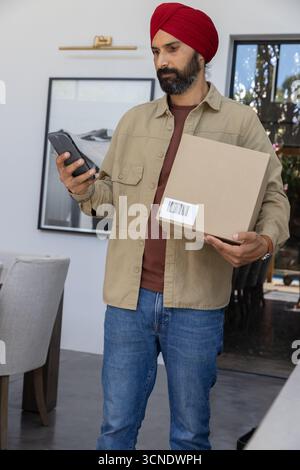 Mid adult indian man with red turban holding package while using scanning device inside dining area Stock Photo