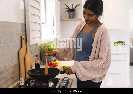 Asian woman stirring wok pan on gas burner in home kitchen near cutting board, copy space Stock Photo