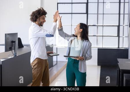 Middle eastern male coworkers high-fiving each other while holding tablets in office Stock Photo