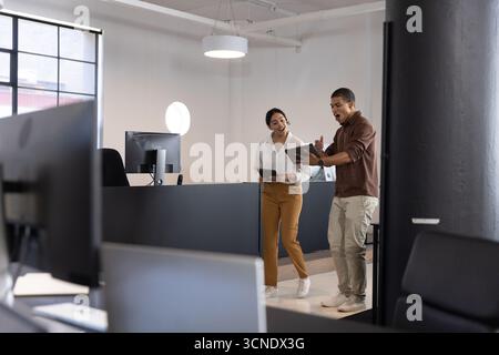 Coworkers holding tablets and reviewing data at modern open-plan office, monitors, copy space Stock Photo