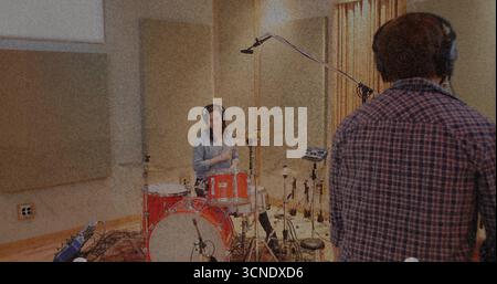 Playing female musician drumming on red drum kit in soundproof studio, with overhead microphones Stock Photo