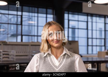 Woman sitting at desk in office listening to colleague while checking monitor and trays Stock Photo
