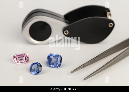 A close up of three different colored gems, including a pink one, and a magnifying glass Stock Photo