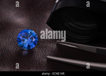 A beautiful blue diamond is placed on a table next to a magnifying glass and a pair of tweezers. The diamond is the center of attention, and the magni Stock Photo