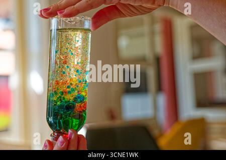 She lifts the bottle upside down and watches colored bubbles rise and fall, pink blue and green move through yellow layers, the playful mix swirls gen Stock Photo
