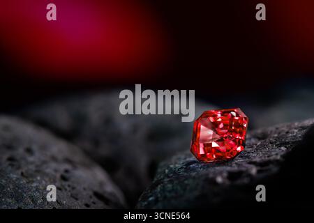 A red gemstone is sitting on a rock. The stone is small and shiny, and it is surrounded by a dark background. The image has a mysterious and intriguin Stock Photo
