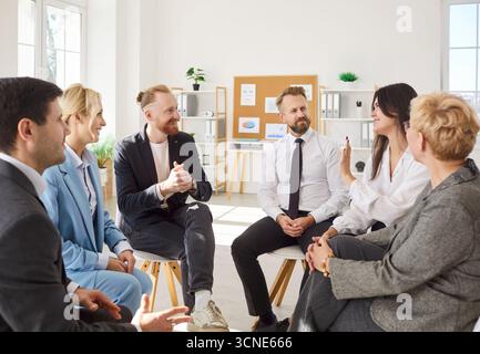 Professionals sitting in circle in office, discussing ideas, enjoying teamwork and collaboration. Stock Photo