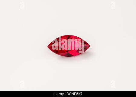A red gemstone is sitting on a white background. The gemstone is a ruby and it is cut into an oval shape Stock Photo