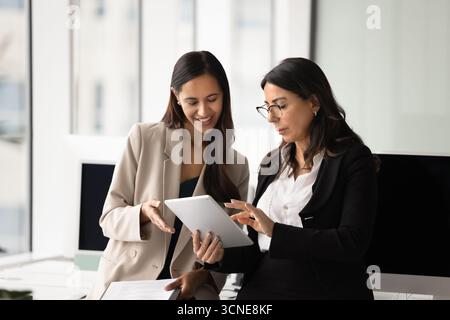 Younger and senior female business colleagues discussing online product Stock Photo