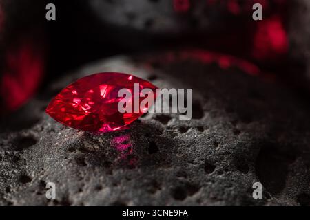A red gemstone is sitting on a rock. The stone is shiny and has a beautiful red color Stock Photo