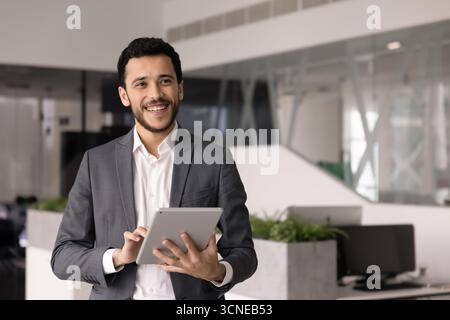 Cheerful young office employee man typing on tablet Stock Photo