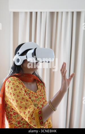 Indian woman wearing yellow kurta, vr headset reaching interface in room, copy space Stock Photo