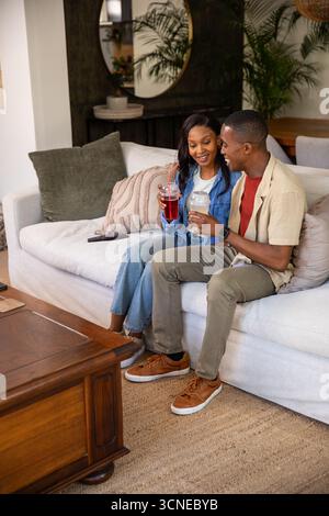 African American men sitting side by side on sofa in living room holding cups with straws Stock Photo