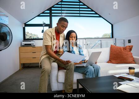 African American colleagues collaborating on light sofa in loft office using laptop and documents Stock Photo