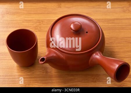 A Japanese or Chinese style clay teapot and a teacup on a wooden tray. A still life concept for a traditional tea ceremony, relaxation, and slow livin Stock Photo