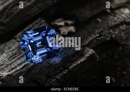 A blue gemstone is sitting on a rock. The stone is large and has a shiny, reflective surface. The image has a moody, mysterious feel to it Stock Photo