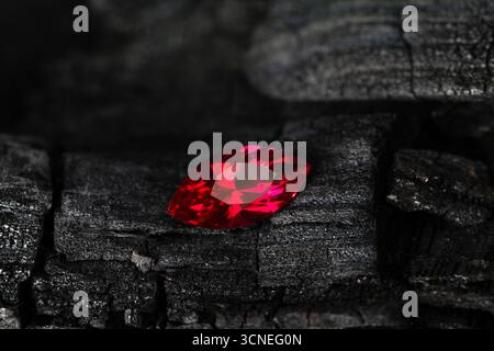 A red gemstone sits on a black surface. The stone is shiny and has a smooth texture. The contrast between the red stone and the black surface creates Stock Photo