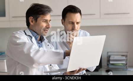 Confident male doctor consulting patient in clinic office using notebook Stock Photo