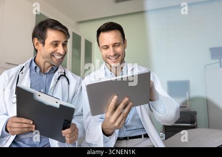 Two cheerful male doctors relax reviewing digital records on tablet Stock Photo