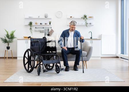 Disabled man practicing walking with a cane in a modern apartment setting Stock Photo