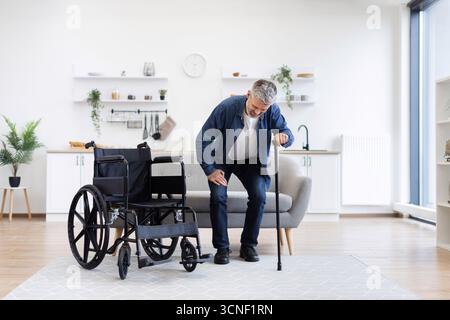 Disabled man practicing walking with cane assistance in home interior setting Stock Photo