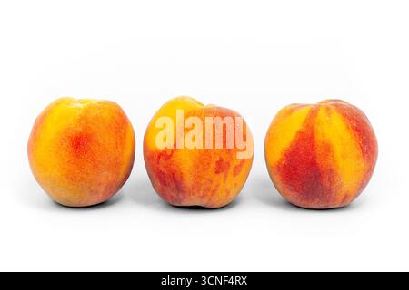Three peaches are shown in a row, with the middle peach being the largest. The peaches are all ripe and ready to eat Stock Photo