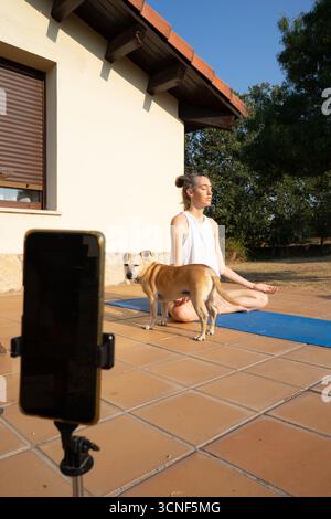 Woman recording online yoga class with her dog next to her Stock Photo