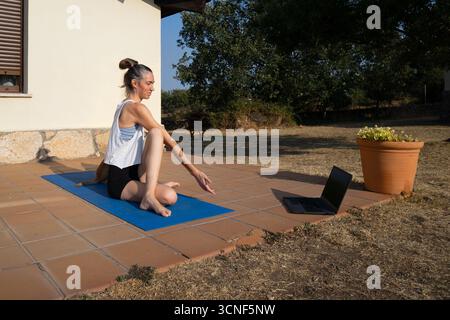 Yoga instructor teaching online yoga class on terrace with laptop Stock Photo