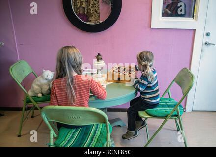 Two small children are sitting at a table and playing games. Stock Photo