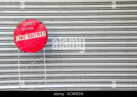 Handmade “NO ENTRY” sign with handwritten text on wire frame in front of closed roller shutter, symbolizing restricted access or privacy. Stock Photo