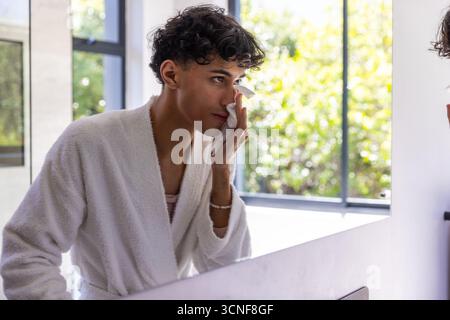 Man wiping face with cloth at bathroom by window mirror and sink, copy space Stock Photo