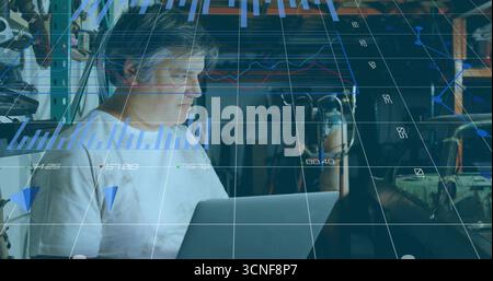 Mature technician analyzing laptop data using holographic charts in cluttered workshop Stock Photo