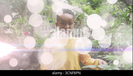 Smiling child wearing yellow shirt standing in backyard garden, with potted plants and umbrella Stock Photo