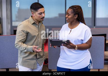 Diverse coworkers collaborating on digital tablet at office near partitioned desks, dividers Stock Photo