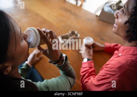 Diverse friends sitting at table at cafe sipping coffee from cups, empty cardboard cup carrier Stock Photo