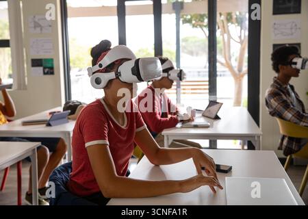 Diverse students using vr headsets training on technology at lab tables with laptops Stock Photo