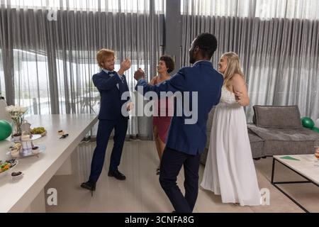 Newlyweds with friends raising champagne flutes near buffet table at lounge in formal attire Stock Photo