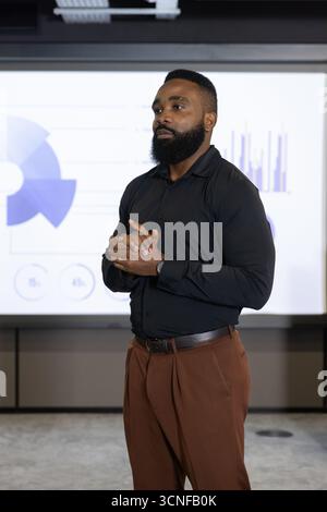 African american man in black shirt presenting charts on projection screen in meeting room Stock Photo